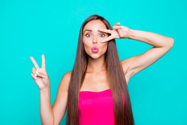 水色の背景の前でピースサインをする女性
