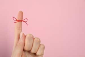 ピンクの背景の前でリボンのかかった人差し指を出す女性の手