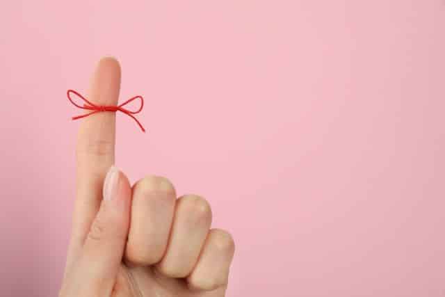 ピンクの背景の前でリボンのかかった人差し指を出す女性の手